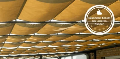 Goldbraune Seilspannmarkise PremiumPlus mit gleichmäßiger Wellenoptik und Aluminiumrohren unter einer Terrassenüberdachung.