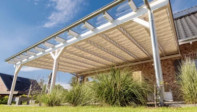 Moderne Terrassenüberdachung mit hellem Sonnenschutzstoff vor einem Wohnhaus im Gartenbereich