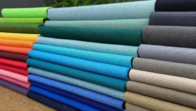 Bunte Stoffmuster in verschiedenen Farben ordentlich gestapelt auf einem Holztisch im Innenbereich.